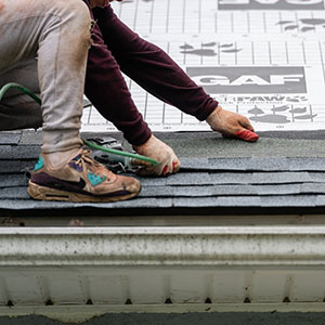 Close up of a worker laying down dark gray GAF shingles on a residential roof