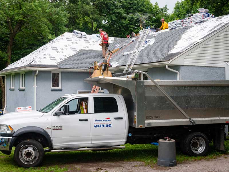 The Thomas Roofing Company crew installing new shingles on a small residential home with one of their company pickup trucks in the foreground