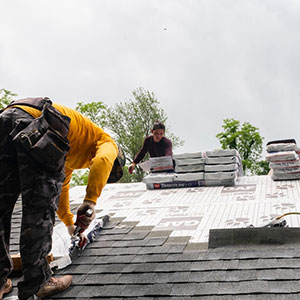 Thomas Roofing Company team members installing new dark gray GAF shingles on a residential roof